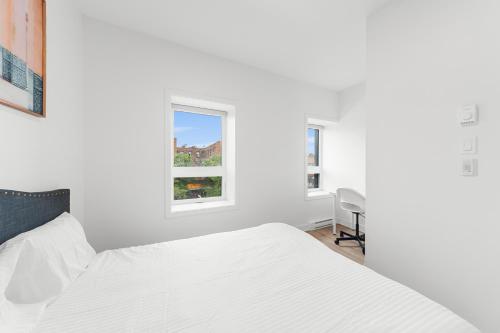 a white bedroom with a bed and a chair at Stonewall Suites in Montréal