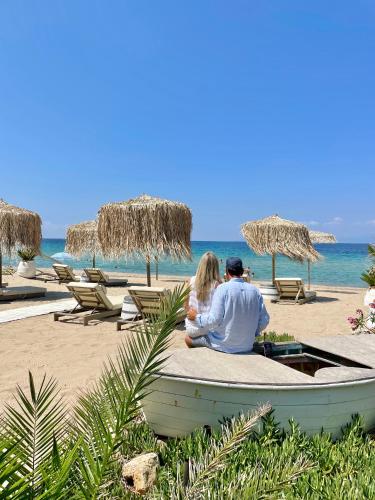 a man and woman sitting on a bench on the beach at Byblos Mare-The Exclusive Beach Front Villa in Skala Sotiros