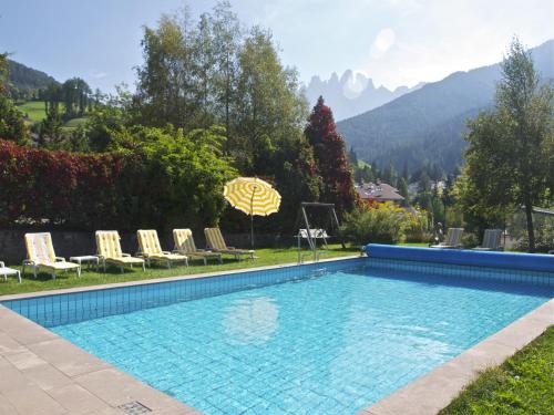 una piscina en un patio con sillas y sombrilla en Hotel Tyrol, en Funes