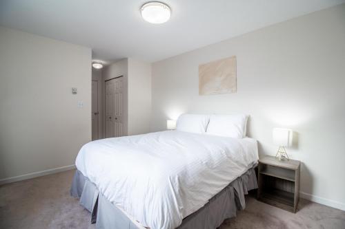 a white bedroom with a large bed and a night stand at NN - Pink Palace - Downtown 1-bed 1-bath in Whitehorse