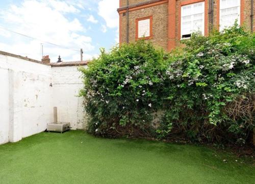 a garden with green grass and a building with a bush at Battersea boutique townhouse in London