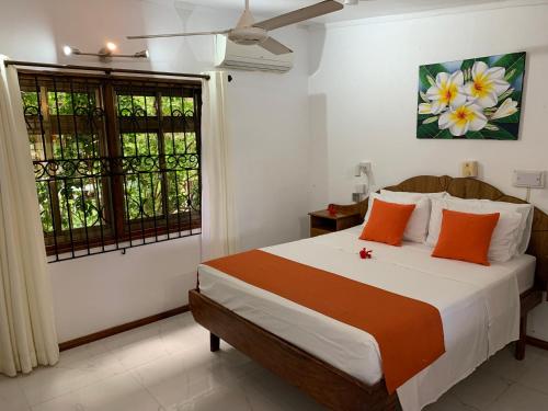 a bedroom with a bed with orange pillows and a window at Amitie Chalets Praslin in Grand Anse