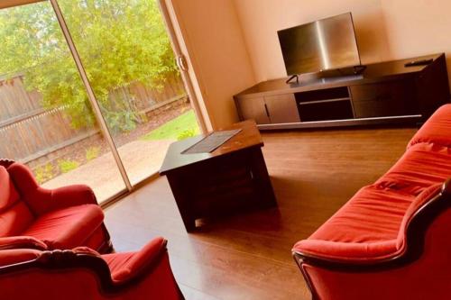 een woonkamer met 2 rode stoelen en een flatscreen-tv bij Charming 4 bedrooms house in Truganina /Williams Landing in Laverton
