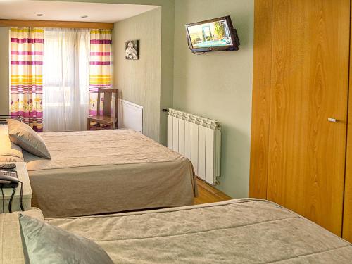 a bedroom with two beds and a tv on the wall at Hostal Real Aranjuez in Aranjuez