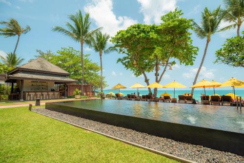 a swimming pool with chairs and umbrellas in front of a resort at Buri Rasa Village Samui in Chaweng