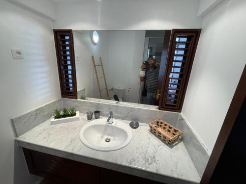 a bathroom sink with a mirror and a person taking a picture at CLANES LOCATION Acerola in La Trinité