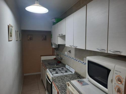 cocina con armarios blancos, fogones y microondas en Depto 3 ambientes zona centro en Mar del Plata