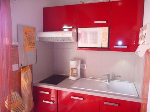 une petite cuisine avec des armoires rouges et un évier dans l'établissement Appartement proche plage avec terrasse, 6 couchages, parking privé, Internet optionnel - FR-1-387-75, à Marseillan