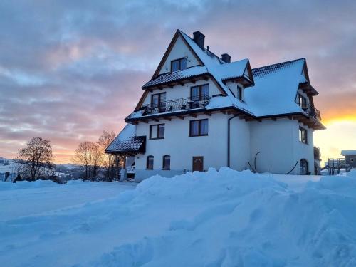 a house covered in snow with the sunset in the background at Pokoje u Hani - sauna, balia z hydromasażem in Bukowina Tatrzańska