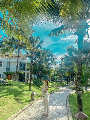 a woman is standing on a sidewalk near a palm tree at Sonata Resort & Spa in Phan Thiet