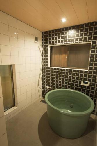 a bathroom with a green tub in a tiled wall at Jikukan Enishi in Taisha