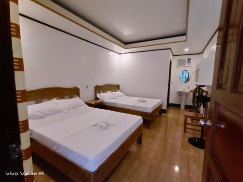 two beds in a room with white walls and wooden floors at Rabang Traveller's Inn in San Vicente