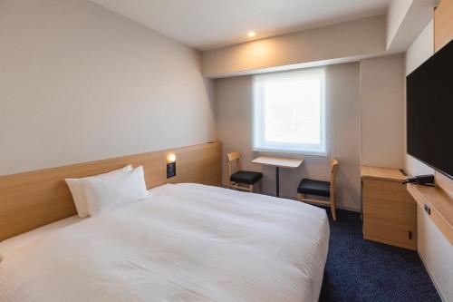 a hotel room with a white bed and a desk at Sotetsu Grand Fresa Kumamoto in Kumamoto