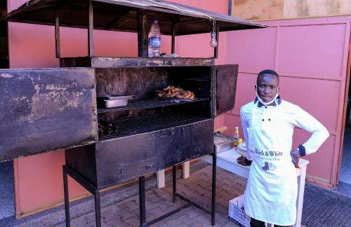 a man standing next to an oven with meat at Precise Motel in Kampala