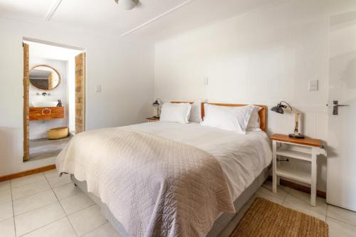 a white bedroom with a bed and a mirror at Arendsig Wine Estate & Cottages in Bonnievale