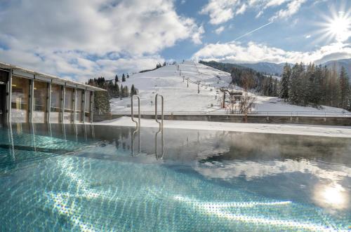 ein Schwimmbad mit einem schneebedeckten Berg im Hintergrund in der Unterkunft Holzhotel Forsthofalm in Leogang