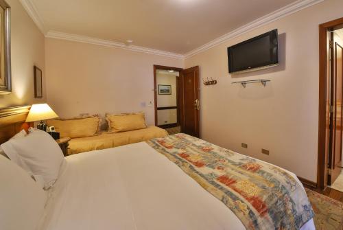 a bedroom with a bed and a television on the wall at Le Suisse Elegance Hotel in Campos do Jordão