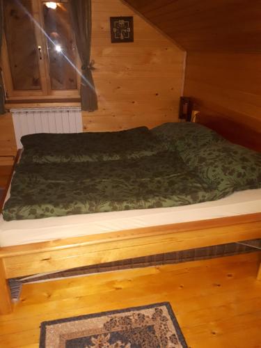 a bed in a wooden room with a green comforter at Holiday Home Tirol in Vlasic
