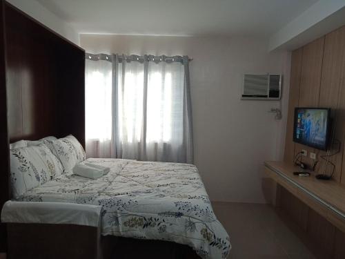 een slaapkamer met een bed en een raam met een televisie bij Cozy1233 studio at The Persimmon in Cebu City