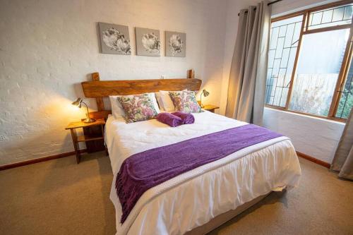 a bedroom with a large bed with purple sheets and a window at 139 Longships - Self Catering Flatlet in Plettenberg Bay