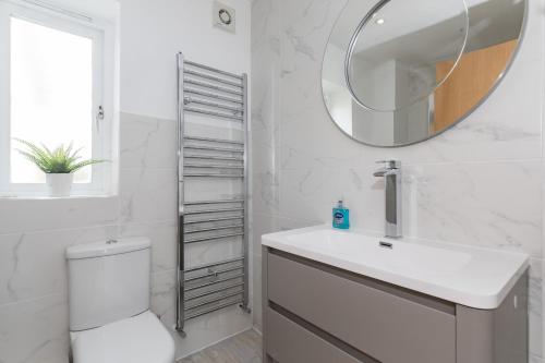 a white bathroom with a toilet and a mirror at Heliodoor Apartments Milton Keynes Spacious 5 Bedroom House with Free Parking, Near M1 J14 in Broughton