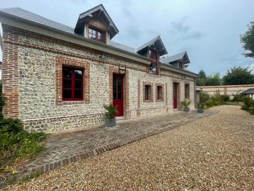 ceglany budynek z czerwonymi drzwiami na żwirowym podjeździe w obiekcie Gîte Les Roches d'Étigues w mieście Vattetot-sur-Mer