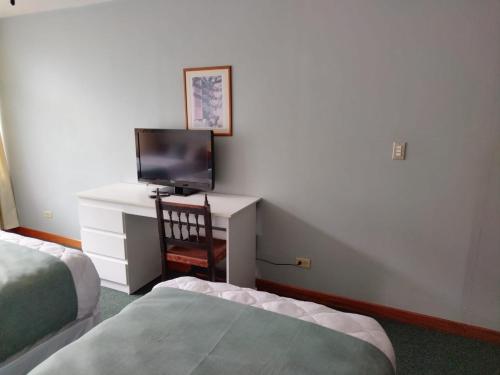 a room with two beds and a desk with a television at Apartotel Tairona in San Pedro