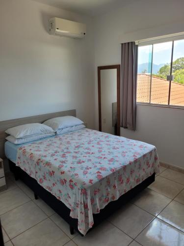a bedroom with a bed with a floral bedspread and a window at Residencial do Angelo - Pinheira in Pinheira