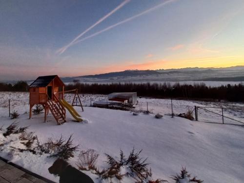 a playground in a snow covered field with the sunset at Domek na Hubce 1 in Maniowy