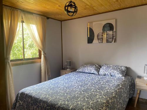 a bedroom with a bed with a blue comforter and a window at Cabañas Santa Cruz, Ubicada a 10 min de la plaza, Piscina , Viñas, Ruta del Vino y mas in Santa Cruz