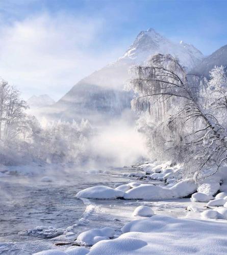 a snow covered mountain in front of a river at Pension Alpina in Roppen