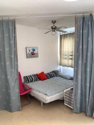 a bed in a room with blue curtains and a ceiling fan at Clarissa Apartment in Costa de Antigua