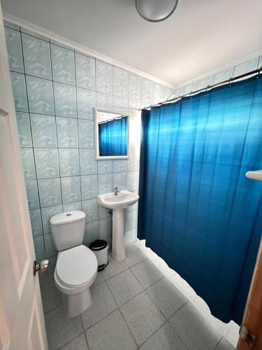 y baño con aseo, lavabo y cortina de ducha azul. en HOSTAL APANANTOR 1 en San Pedro de Atacama