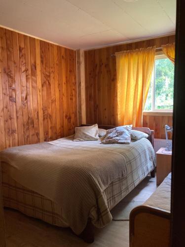 a bedroom with a bed with wooden walls and a window at Hostal Flor del Meli in Dalcahue