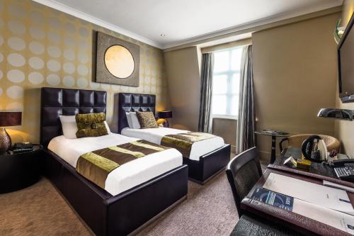 ロンドンにあるワシントン メイフェア ホテルのベッド2台とデスクが備わるホテルルームです。