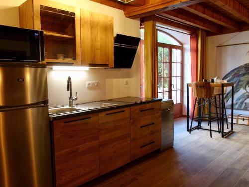 une cuisine avec des armoires en bois et un réfrigérateur en acier inoxydable dans l'établissement Charmant gîte près du Mans : calme, confort, commerces à proximité, idéal pour 2 pers. - FR-1-410-273, à Cérans-Foulletourte