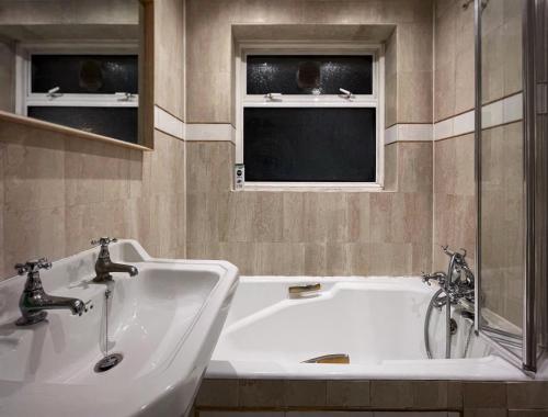 Vintage 3 Bedroom House near Catford في لندن: حمام مع حوض ومغسلة ونوافذ