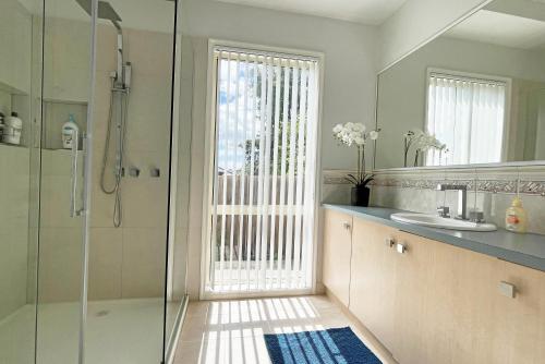 y baño con ducha, lavabo y espejo. en Spacious 5BR House in Hallam near Bunjil Place, en Hallam