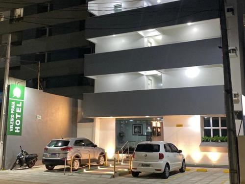 Dos coches aparcados delante de un edificio por la noche. en Veleiro Hotel MCZ, en Maceió