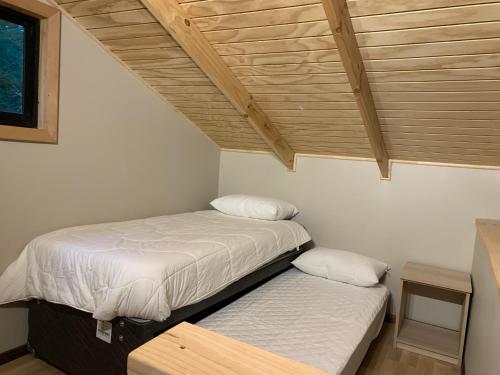 two beds in a room with a wooden ceiling at Cabañas Alto Bosque in Pucón