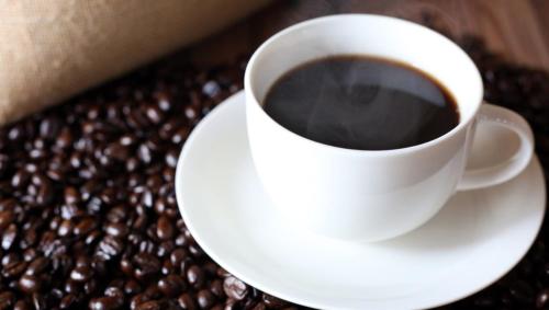 a cup of coffee sitting on a plate next to coffee beans at HOTEL VISCHIO TOYAMA in Toyama
