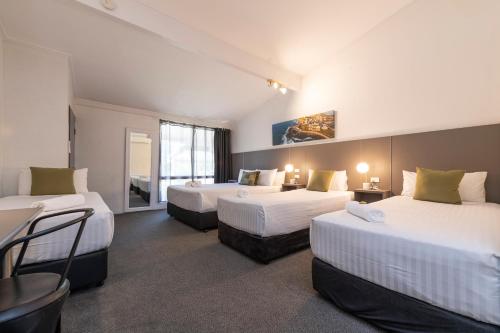 a hotel room with three beds and a table at Fern Bay Motel in Newcastle