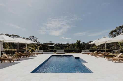 a swimming pool with lounge chairs and umbrellas at The Woods Farm Jervis Bay in Tomerong
