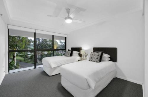 a white bedroom with two beds and a window at Gemini Court - Hosted by Burleigh Letting in Gold Coast