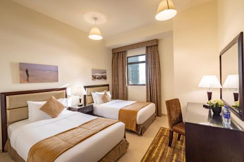 a hotel room with two beds and a desk at Roda Amwaj Suites Jumeirah Beach Residence in Dubai