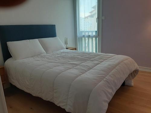 un grand lit blanc dans une chambre avec une fenêtre dans l'établissement Appartement T3 rénové à 10 min du centre-ville avec balcon, garage et WIFI à Saint-Jean-de-Luz - FR-1-239-584, à Saint-Jean-de-Luz
