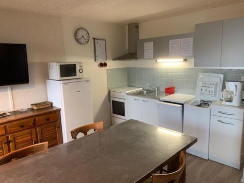 une cuisine avec des appareils blancs et une table avec des chaises dans l'établissement F2 bis tout confort avec balcon au pied des pistes, parking et local à skis, Mont-Dore - FR-1-415-100, à Le Mont-Dore