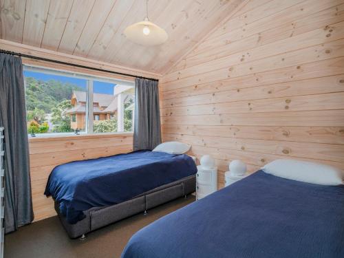 two beds in a room with wooden walls and a window at Ocean Beach Beauty - Tairua Holiday Home in Tairua