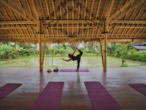 a woman doing a yoga pose in a room with purple mats at Nandini Jungle by Hanging Gardens in Payangan