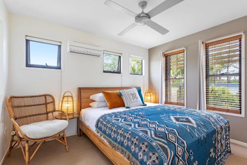 a bedroom with a bed and a chair and windows at Little Whale House in Mudjimba